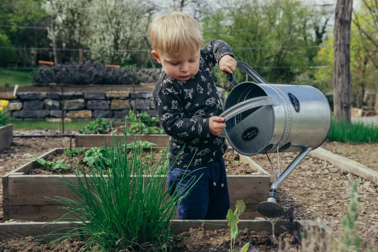 Image of young boy holding a container watering a urban garden.